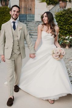 a bride and groom holding hands walking down the street in front of some steps with flowers