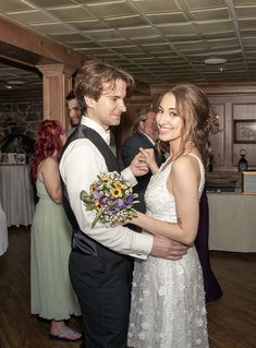 a man and woman standing next to each other in a room with people on the dance floor