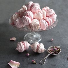 a glass bowl filled with pink meringue cookies next to dried rose petals on a table