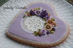 a heart shaped cookie decorated with purple flowers and lace on a white doily plate