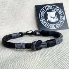 a black and gray rope bracelet with an emblem on the front, sitting next to a card