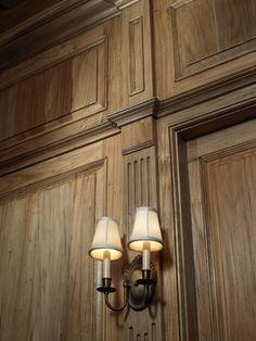 two lamps are on the wall in front of wood paneled walls and door handles