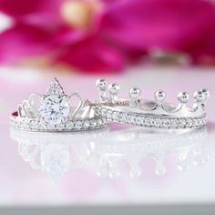 two wedding rings with tiaras on them sitting next to each other in front of pink flowers