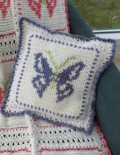 two crocheted pillows sitting on top of a blue chair next to a window