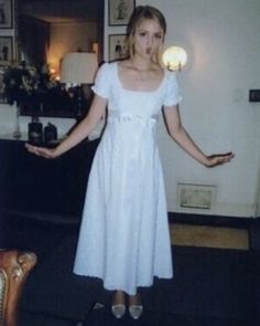 a woman in a white dress is standing with her hands out to the side,