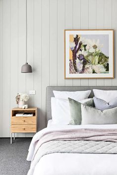 a bed with white sheets and pillows in a bedroom next to a painting on the wall