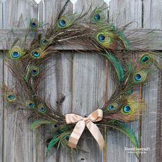 a wreath with peacock feathers is hanging on a wooden fence and it has a bow