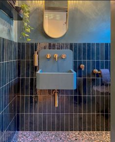 a bathroom with blue tiled walls and a mirror on the wall above it is a sink that has two faucets in front of it