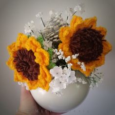 a hand holding a white vase filled with flowers