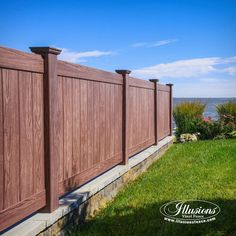 a large wooden fence on the side of a grassy field next to an ocean and blue sky