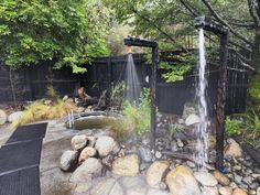 an outdoor shower in the middle of a garden with rocks and water coming out of it