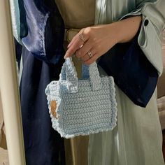 a woman is holding a crocheted purse in her left hand and wearing a ring