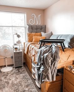 a bed room with a neatly made bed next to a window and a fan in the corner