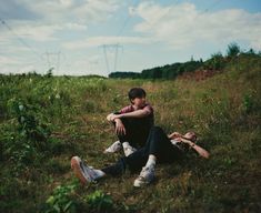 two people sitting on the ground with their arms around each other in a grassy field