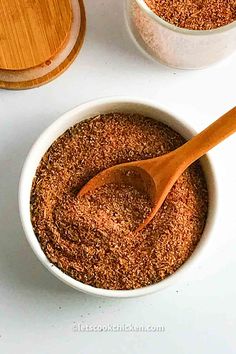 two bowls filled with spices next to wooden spoons on top of a white table