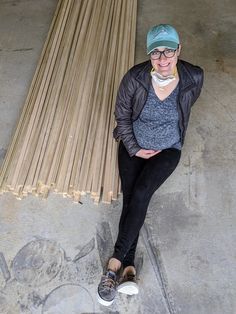 a woman sitting on top of a wooden bench next to a pile of bamboo sticks