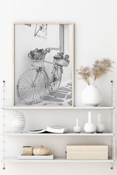 two white shelves with books, vases and flowers on them in front of a black and white photo