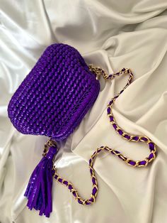 a purple handbag laying on top of a white bed with a chain around it