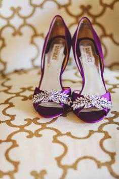 a pair of purple high heeled shoes on top of a white and gold bed