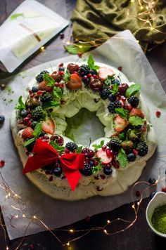 a cake decorated with berries and leaves on top of a wooden table next to a cup of green tea