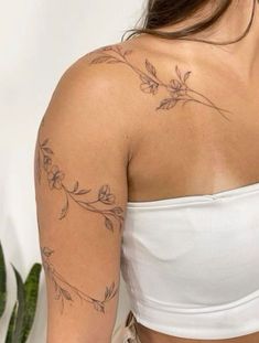 a woman wearing a white crop top with tattoos on her arms and shoulder is looking at the camera