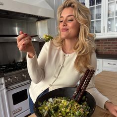 a woman holding a pan filled with food on top of a wooden table