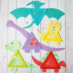 colorful paper cut outs with different shapes and sizes on white wooden boards, including dinosaurs