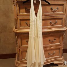 a white dress hanging on a dresser next to a wooden drawer with drawers in it