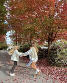 two girls are walking down the street in front of trees with red leaves on them