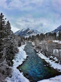 a river surrounded by snow covered trees and mountains in the distance with blue water running through it