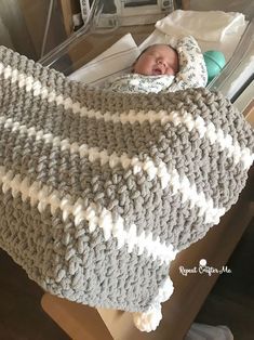 a baby sleeping in a crocheted blanket on top of a bed