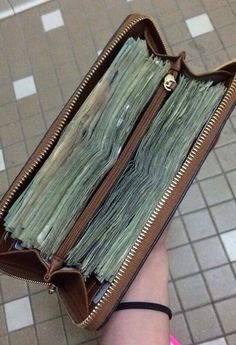 a person is holding a purse full of money in their hand on the tile floor