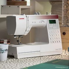 a white sewing machine sitting on top of a table next to a cup of coffee