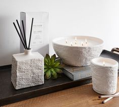 two white candles sitting on top of a table next to a book and planter