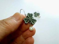 a pair of shamrock earrings with pearls in the foreground and a hand holding it