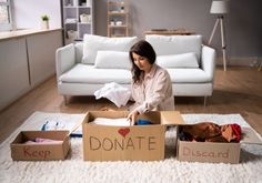 a woman sitting on the floor in front of cardboard boxes with donations written on them