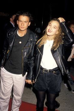 a man and woman are walking down the street holding each other's hands as they both wear black leather jackets