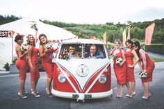 a group of women in red dresses standing next to a vw bus