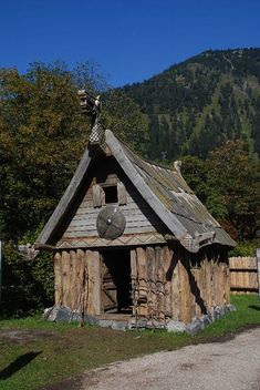 a small wooden structure with a roof made out of logs and wood, in front of a mountain