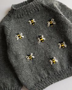 two sweaters with bees on them sitting next to each other, one is grey and the other is yellow