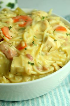 a white bowl filled with pasta and meat on top of a blue table cloth next to a fork