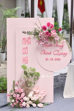 a pink sign with flowers on it sitting in front of a white table cloth and chair