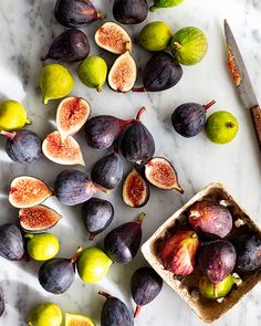 figs and other fruit on a marble counter top with a knife next to them