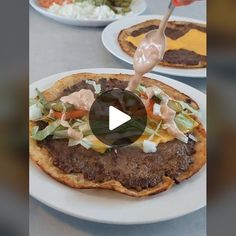 a person pouring dressing on top of a flatbread with meat and vegetables in the background