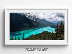 a framed photograph of a lake surrounded by mountains and trees with the words frame tv art above it