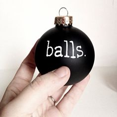 a hand holding a black ornament with the word balls written on it