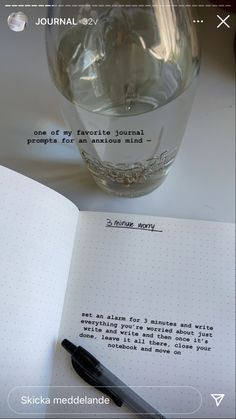 an open notebook with a pen on top of it next to a clear glass vase