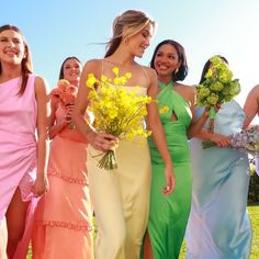 a group of women standing next to each other holding bouquets of yellow and pink flowers