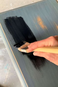 a person holding a paintbrush in their right hand and painting the top of a table