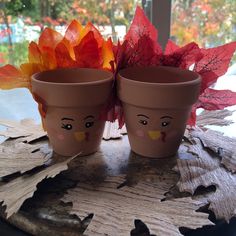 two flower pots with faces painted on them sitting on a table next to some leaves